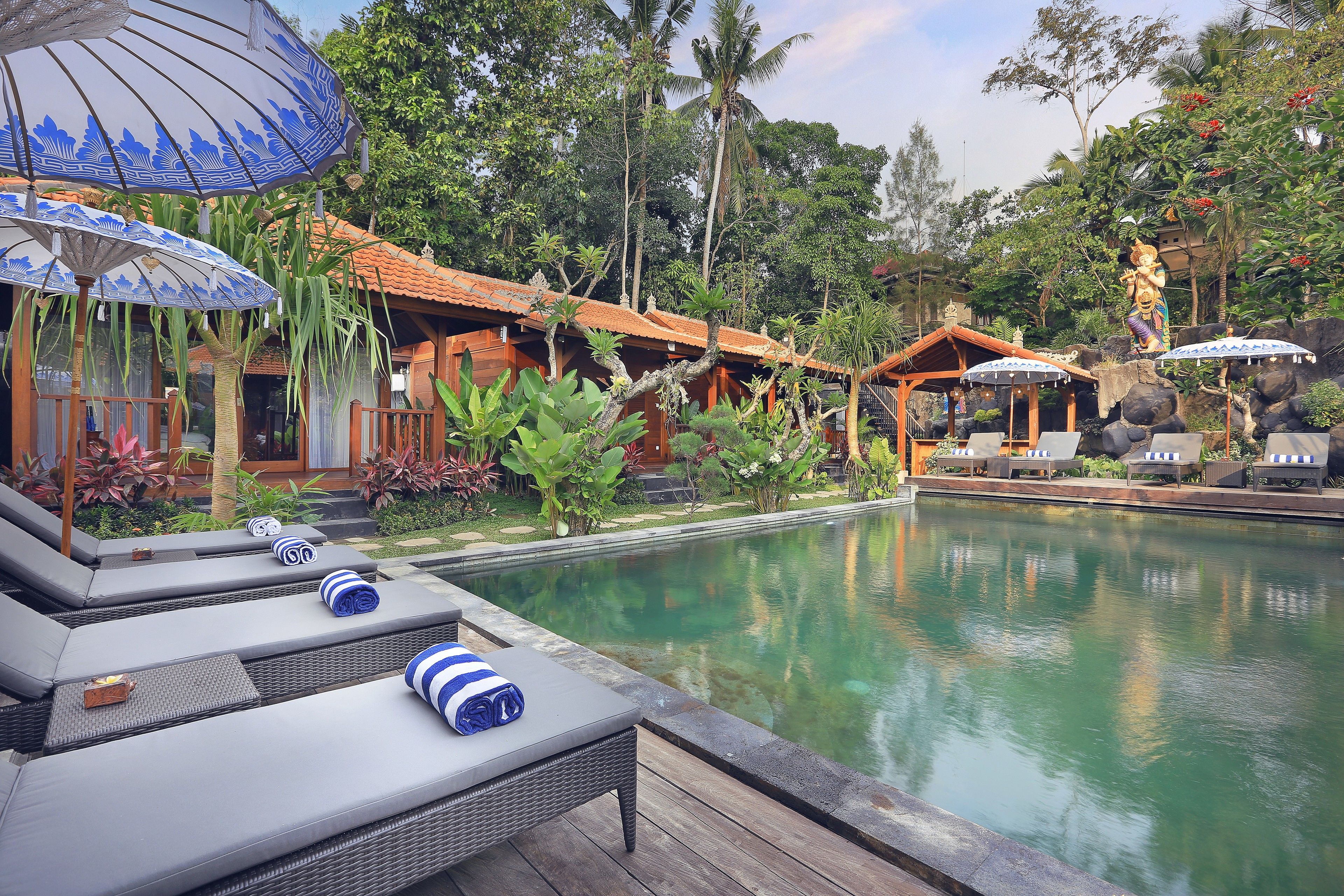 A poolside area with lounge chairs, umbrellas, and a tropical garden setting.