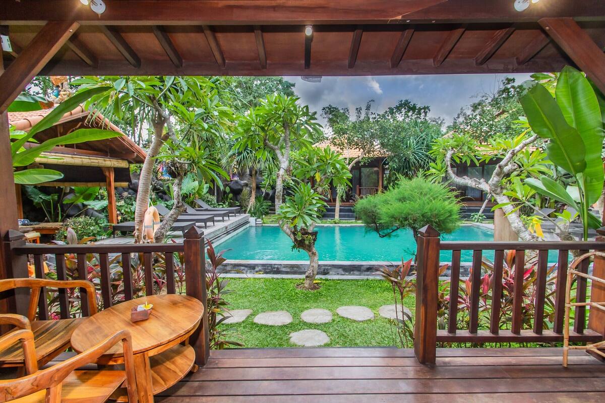 A wooden deck with a pool, surrounded by tropical plants and a small garden area.