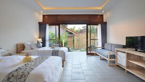 A modern hotel room with two beds, a TV, and a balcony with a view of a garden and a traditional house. - Batu Agung Villas (Ubud)
