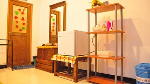 A room with a wooden dresser, a white refrigerator, a wooden shelf unit, and a blue laundry basket. - Sigiri Saman Homestay (Sigiriya)