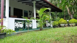 A covered porch with white columns, a green railing, and lush greenery surrounding the area. - Sigiri Saman Homestay (Sigiriya)