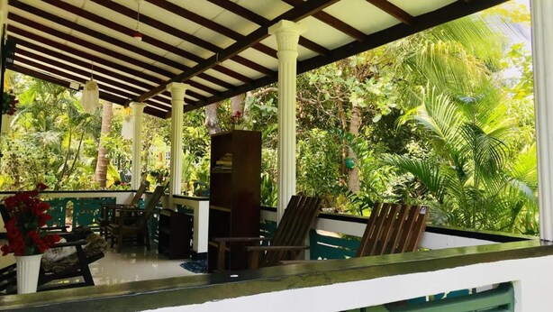 A covered outdoor area with a wooden ceiling, white columns, and lush greenery visible through the sides. - Sigiri Saman Homestay (Sigiriya)