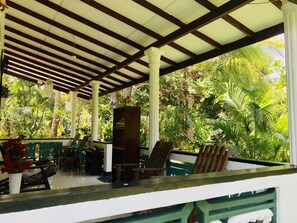 A covered outdoor area with a wooden ceiling, white columns, and lush greenery visible through the sides. - Sigiri Saman Homestay (Sigiriya)