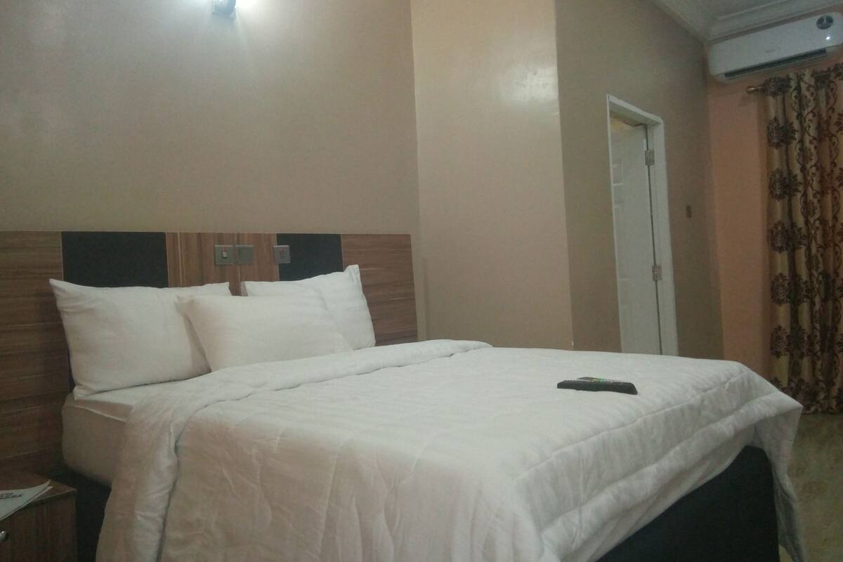A hotel room with a bed, a nightstand, a door, and an air conditioning unit.