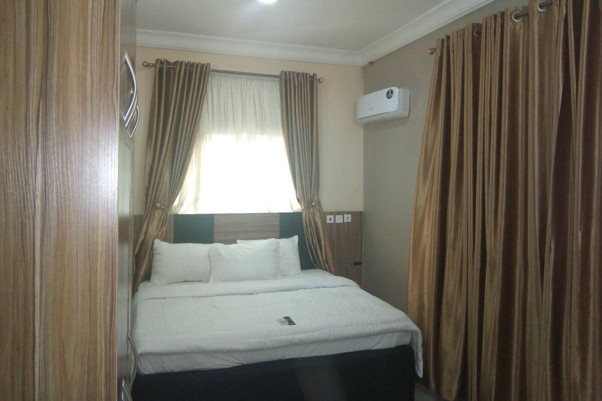A hotel room with a bed, curtains, an air conditioning unit, and a window.