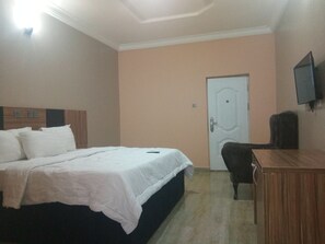 Quarto de hotel com cama, escrivaninha, cadeira, televisão e porta.
