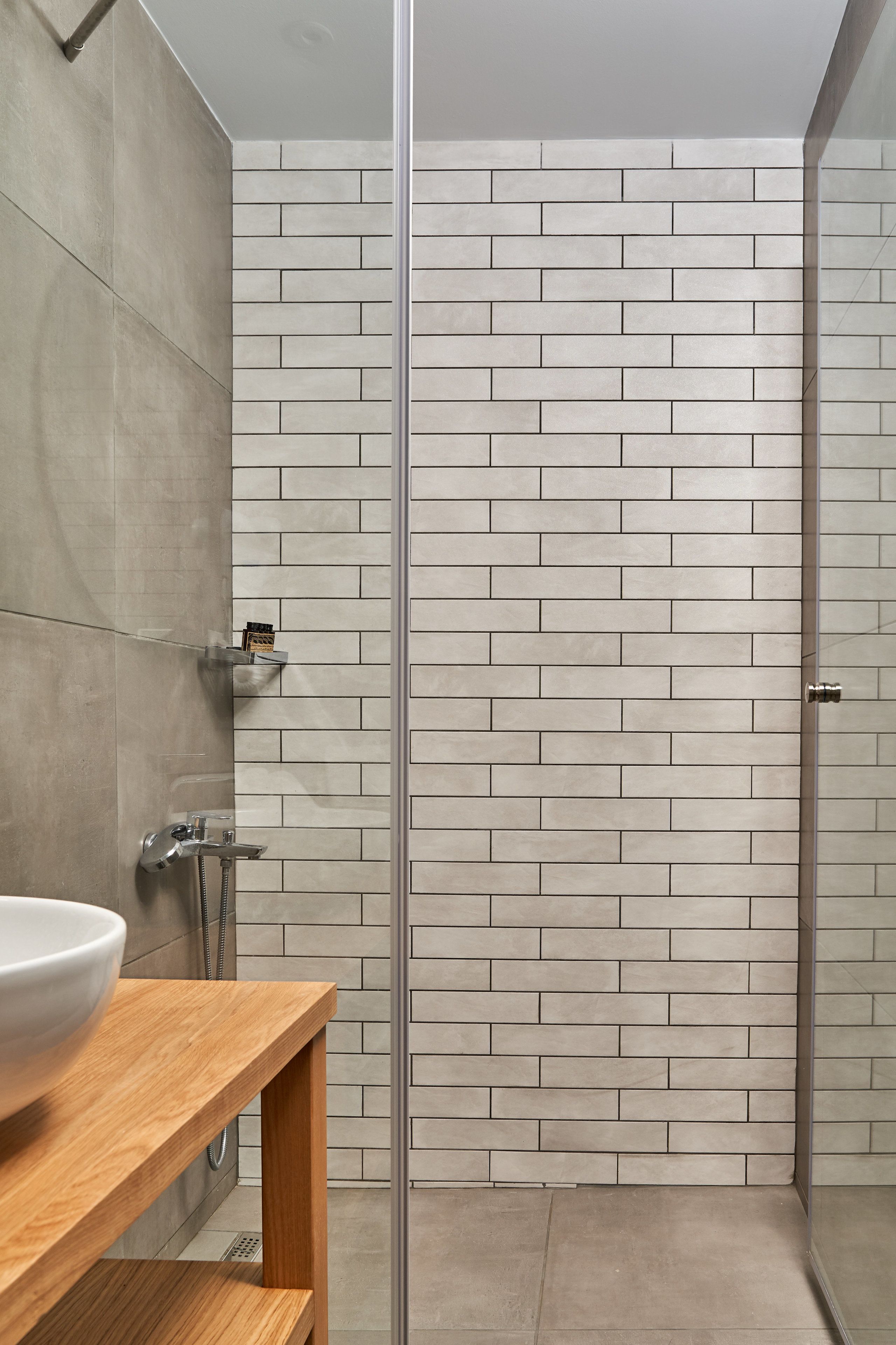 Un baño moderno con cabina de ducha de vidrio, tocador de madera y salpicadero de azulejos.