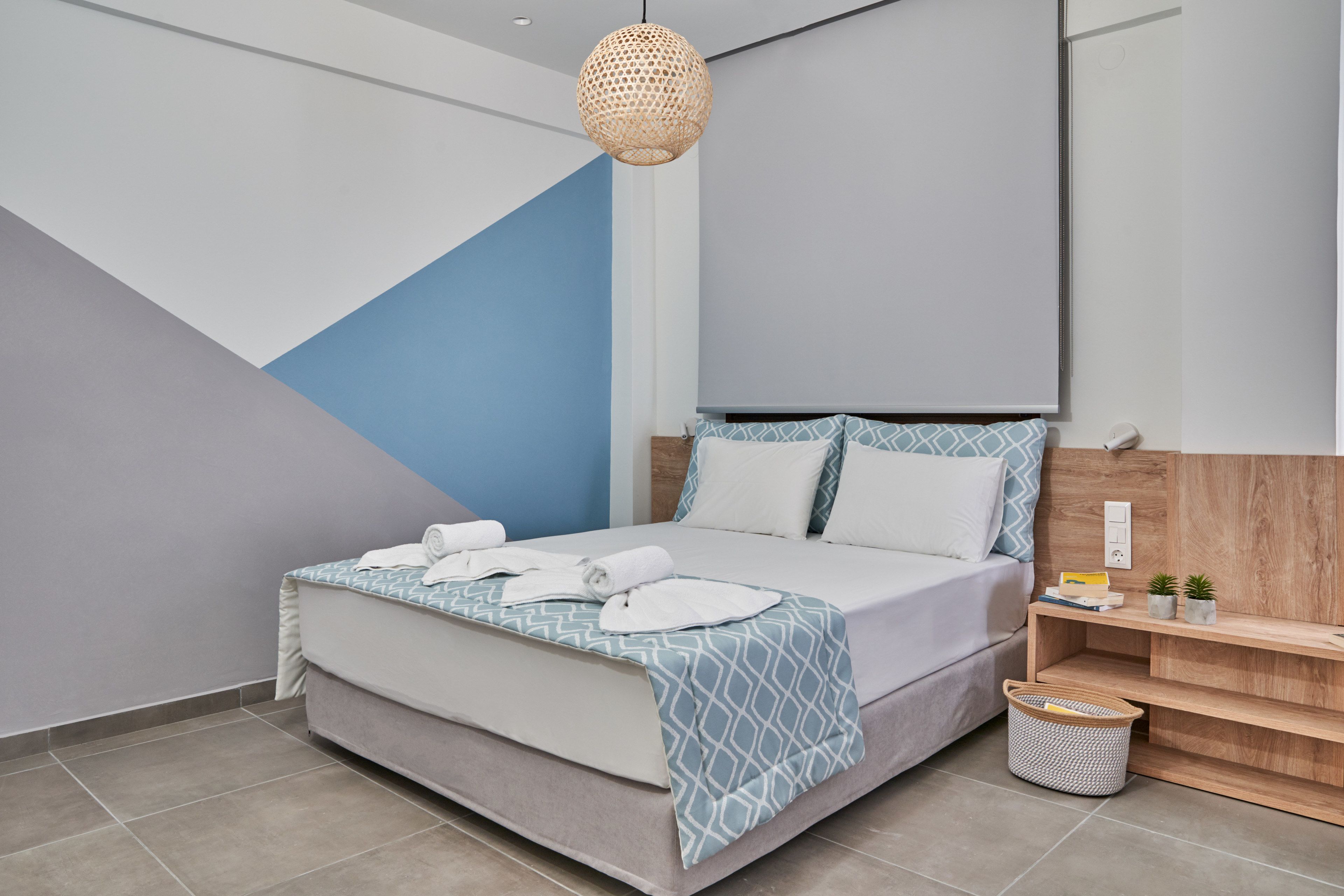 A modern bedroom with a bed, a bedside table, a wall-mounted shelf, and a hanging light fixture.