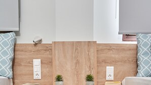 A modern room with a wooden headboard, bedside tables, a small potted plant, a basket with books, and a wall socket.