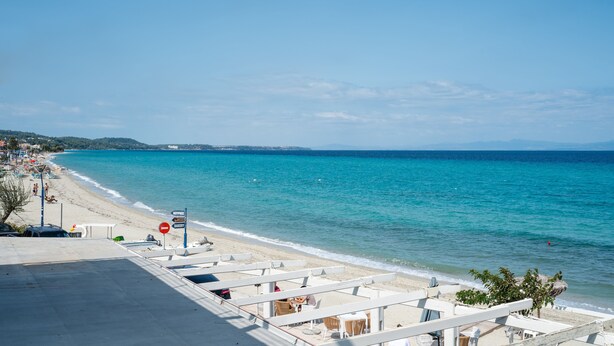 A beachside hotel with a view of the sea, outdoor seating, and a clear sky.
