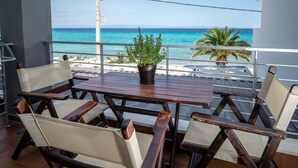 A wooden table with chairs and a potted plant on a balcony overlooking a beach.