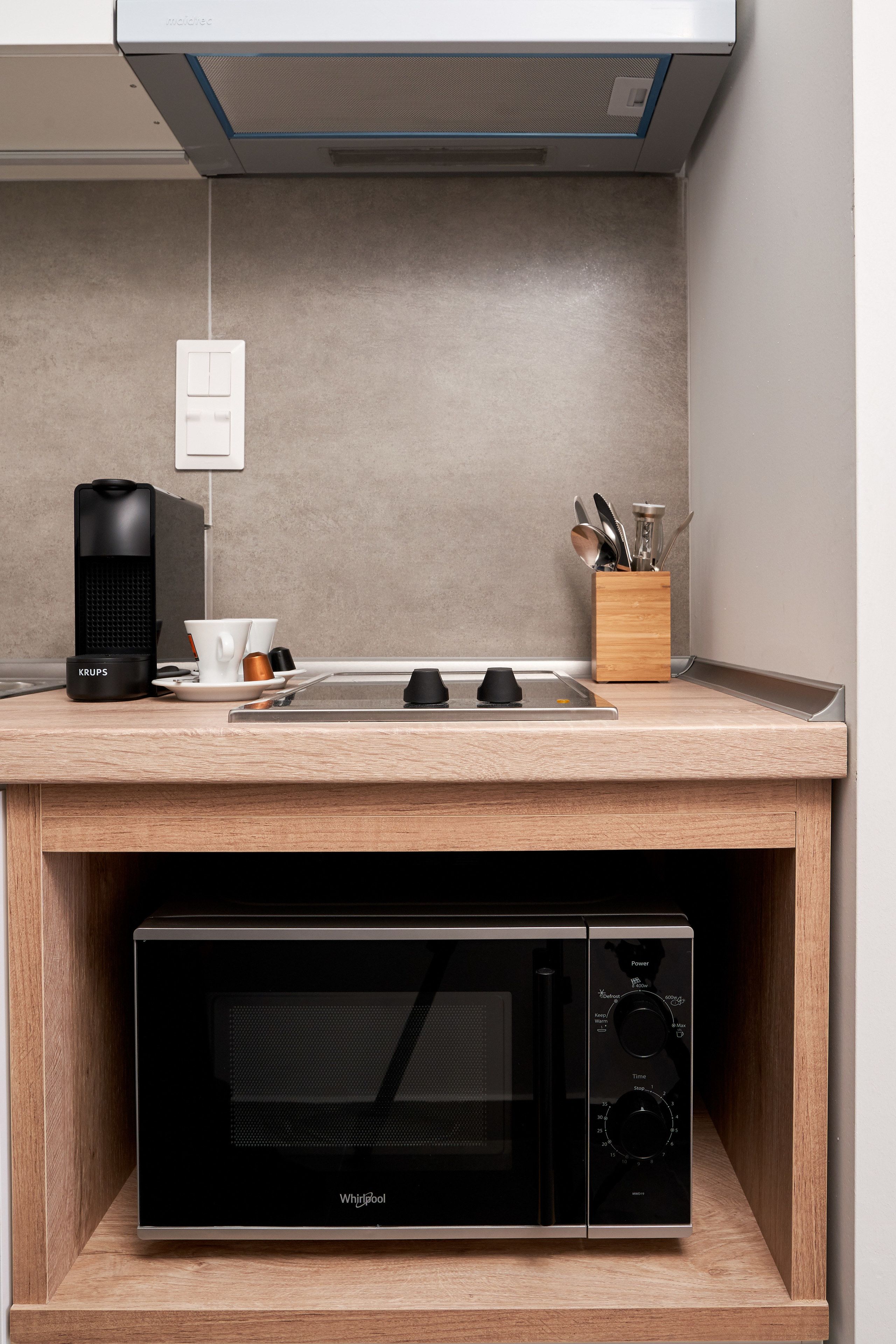 A compact kitchen with a built-in microwave and coffee maker, a wooden countertop, and a knife block.