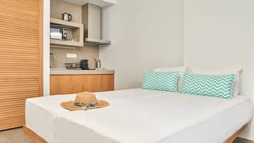 A bedroom with a bed, a wooden wardrobe, a kitchenette with a microwave, a kettle, and a sink.