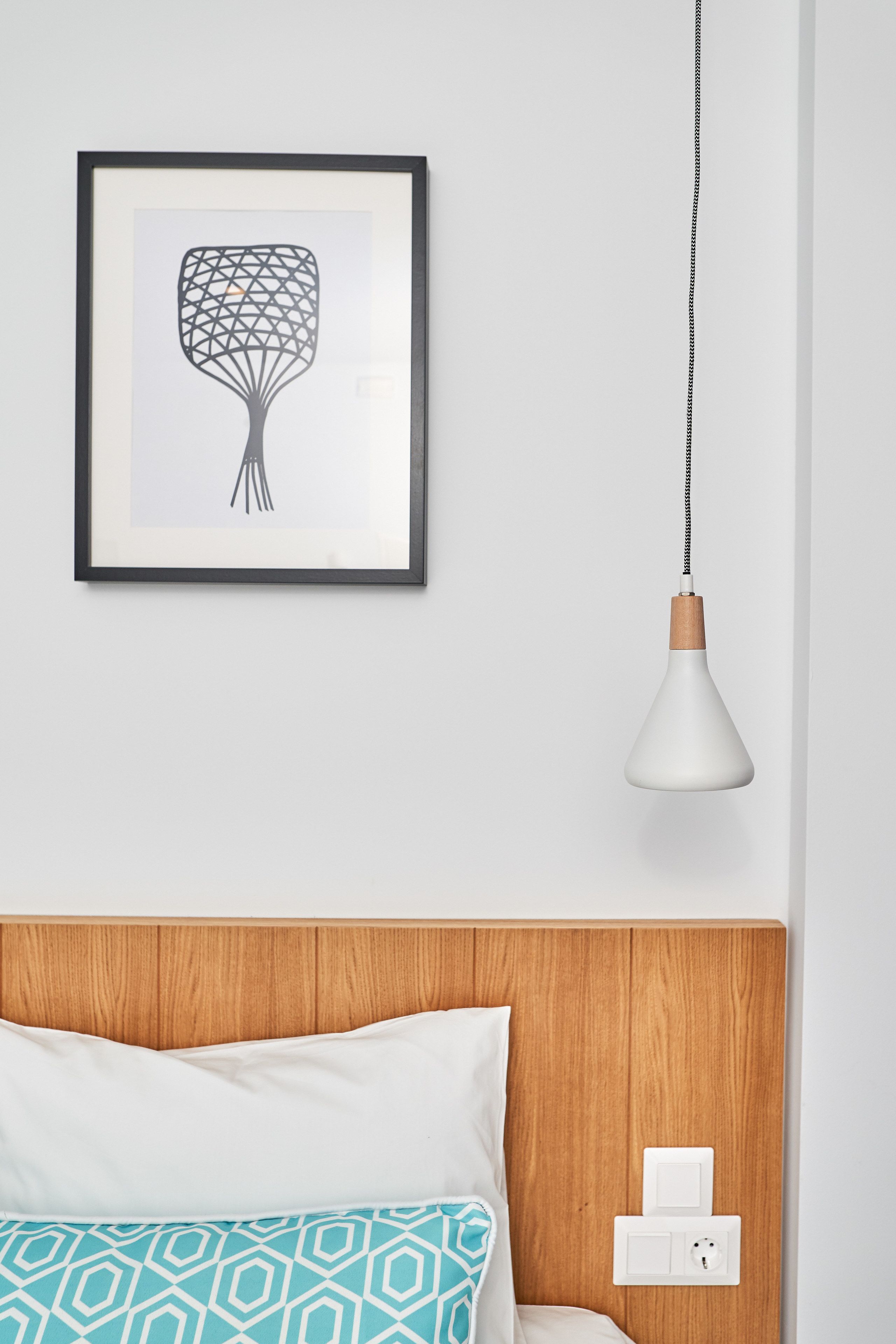 Camera da letto con testiera in legno, una tela astratta incorniciata, una lampada a sospensione bianca e un comodino con presa di corrente.