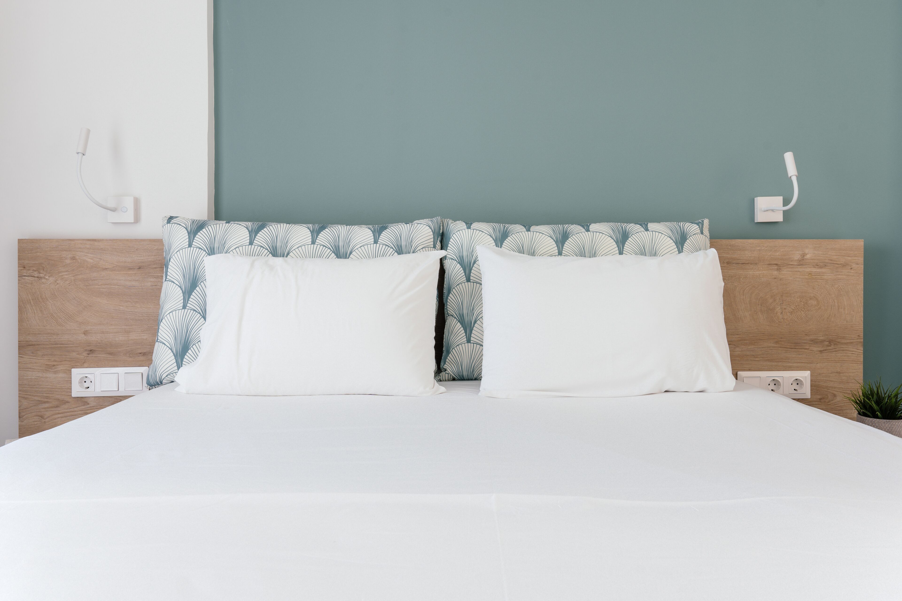 A neatly made bed with white bedding and a patterned headboard.