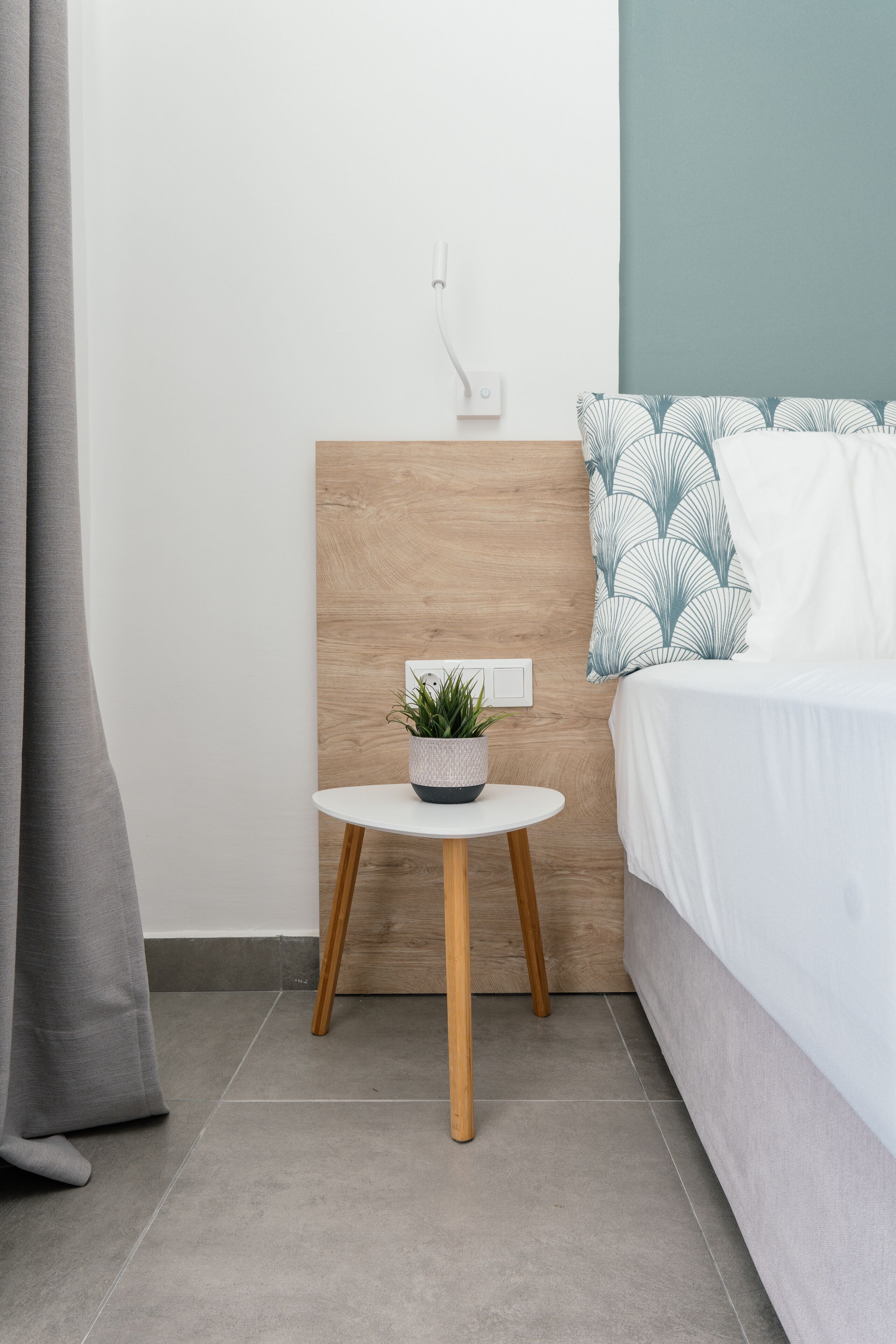 A modern bedroom with a bed, a bedside table with a plant, and a wooden headboard.