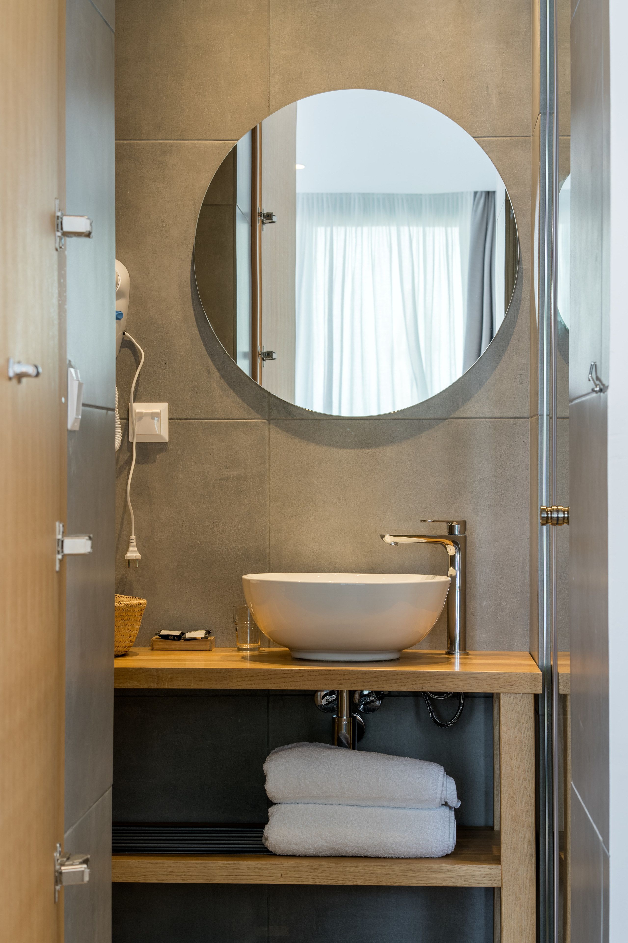 Un baño moderno con un espejo redondo, un lavabo blanco y un perchero para toallas.