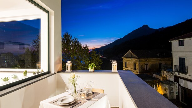 A balcony with a table set for dining, overlooking a mountainous landscape and a body of water. - AmbroSea Amalfi Coast (Vietri sul Mare)