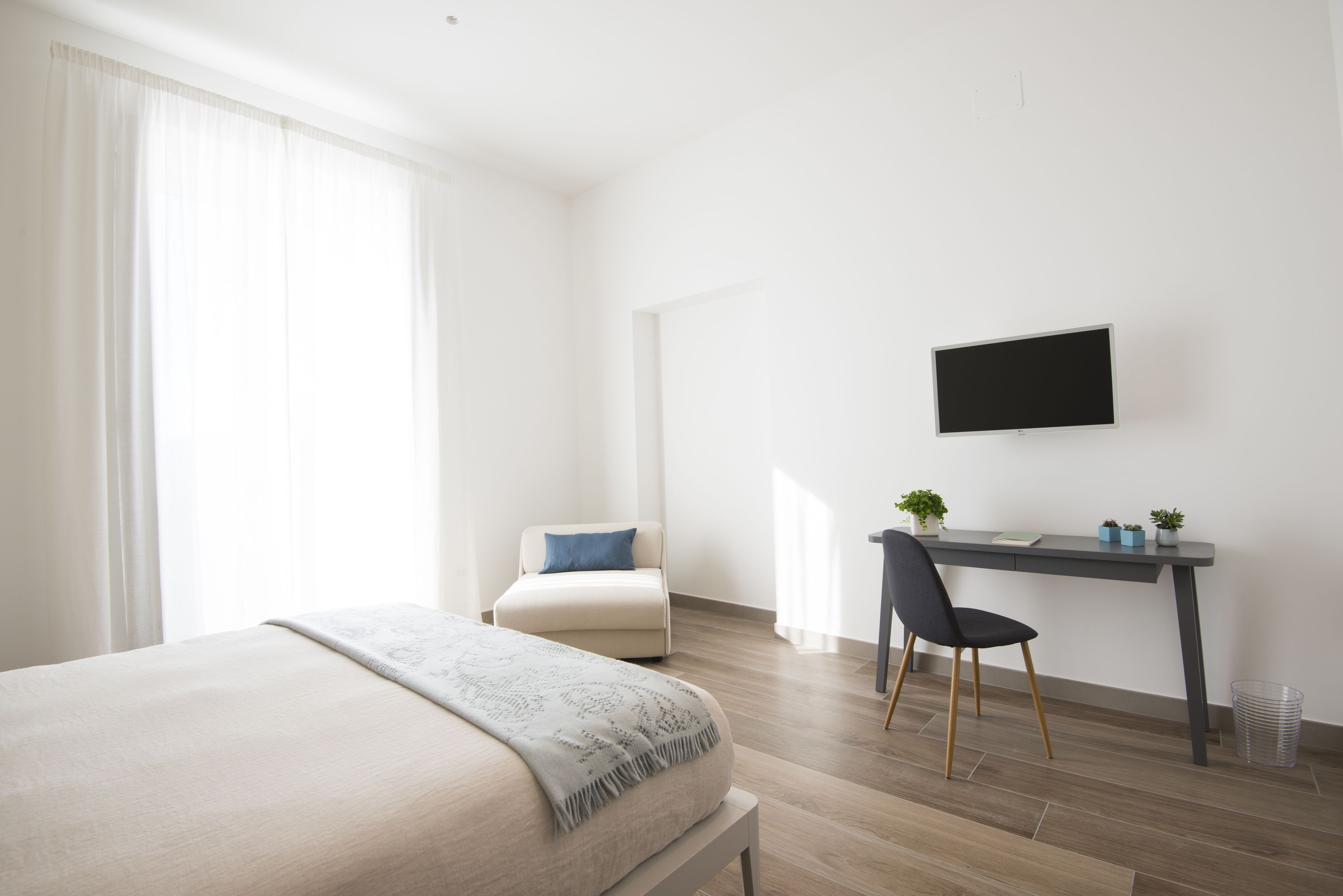 Ett modernt hotellrum med en säng, ett skrivbord med en stol, en tv och ett fönster med gardiner.