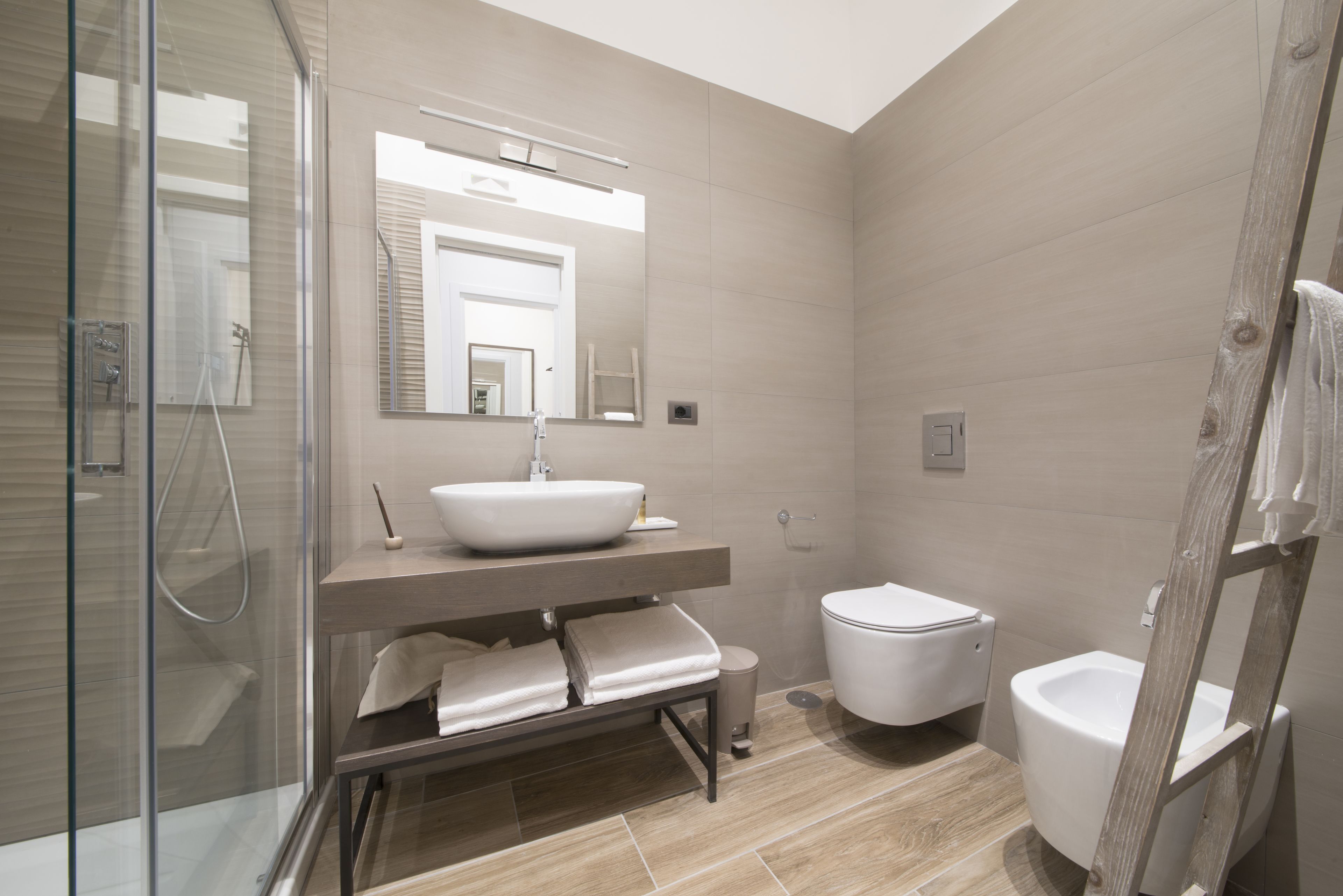 Un baño moderno con cabina de ducha de vidrio, un espejo grande, lavabo sobre encimera, inodoro y bidé.