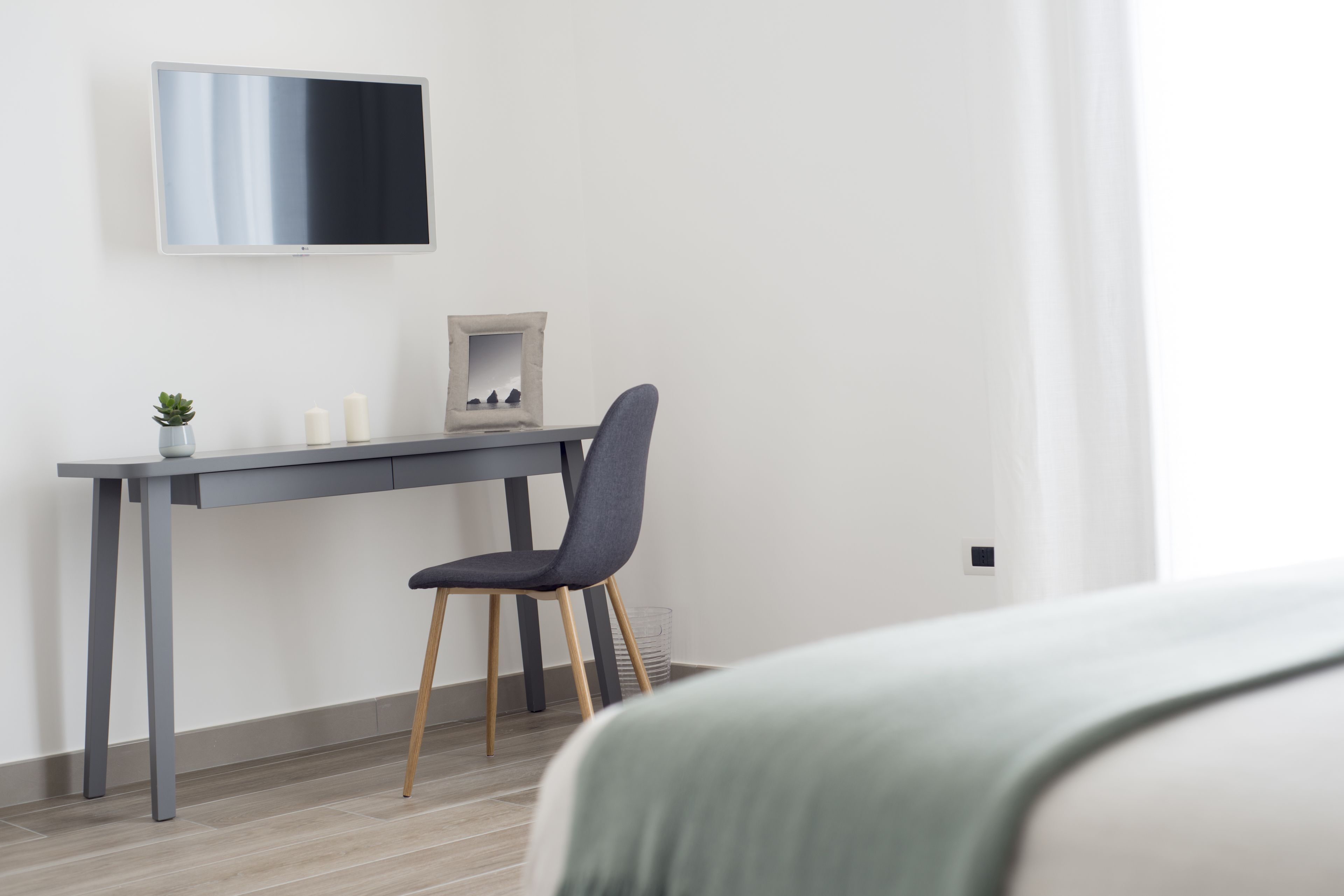 A modern room with a grey desk, a chair, a small plant, and a framed picture.