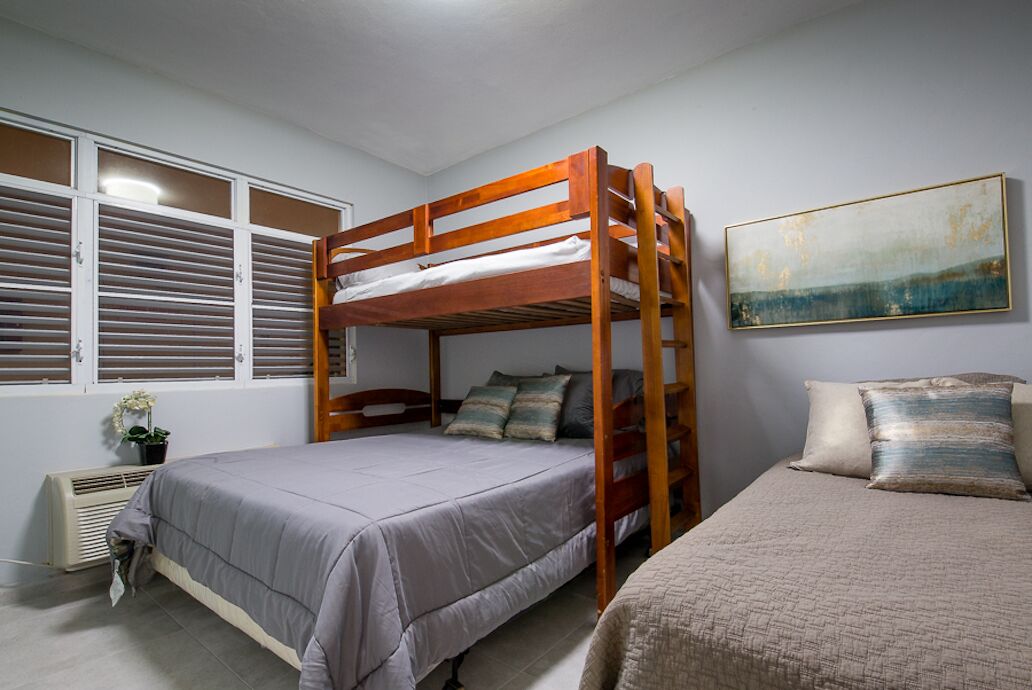 A bunk bed room with a radiator, a window with blinds, and a painting on the wall.