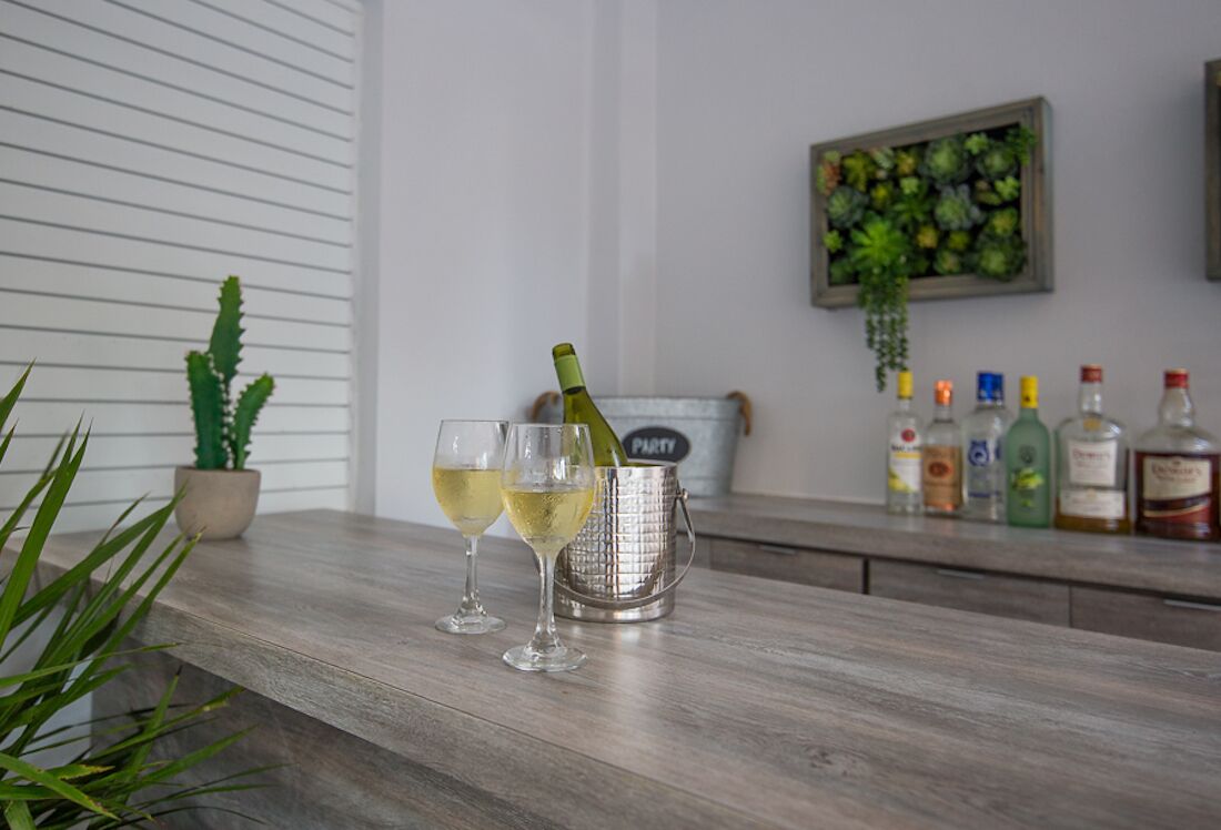 A bar area with two glasses of white wine, a bottle of champagne, and a variety of liquor bottles.