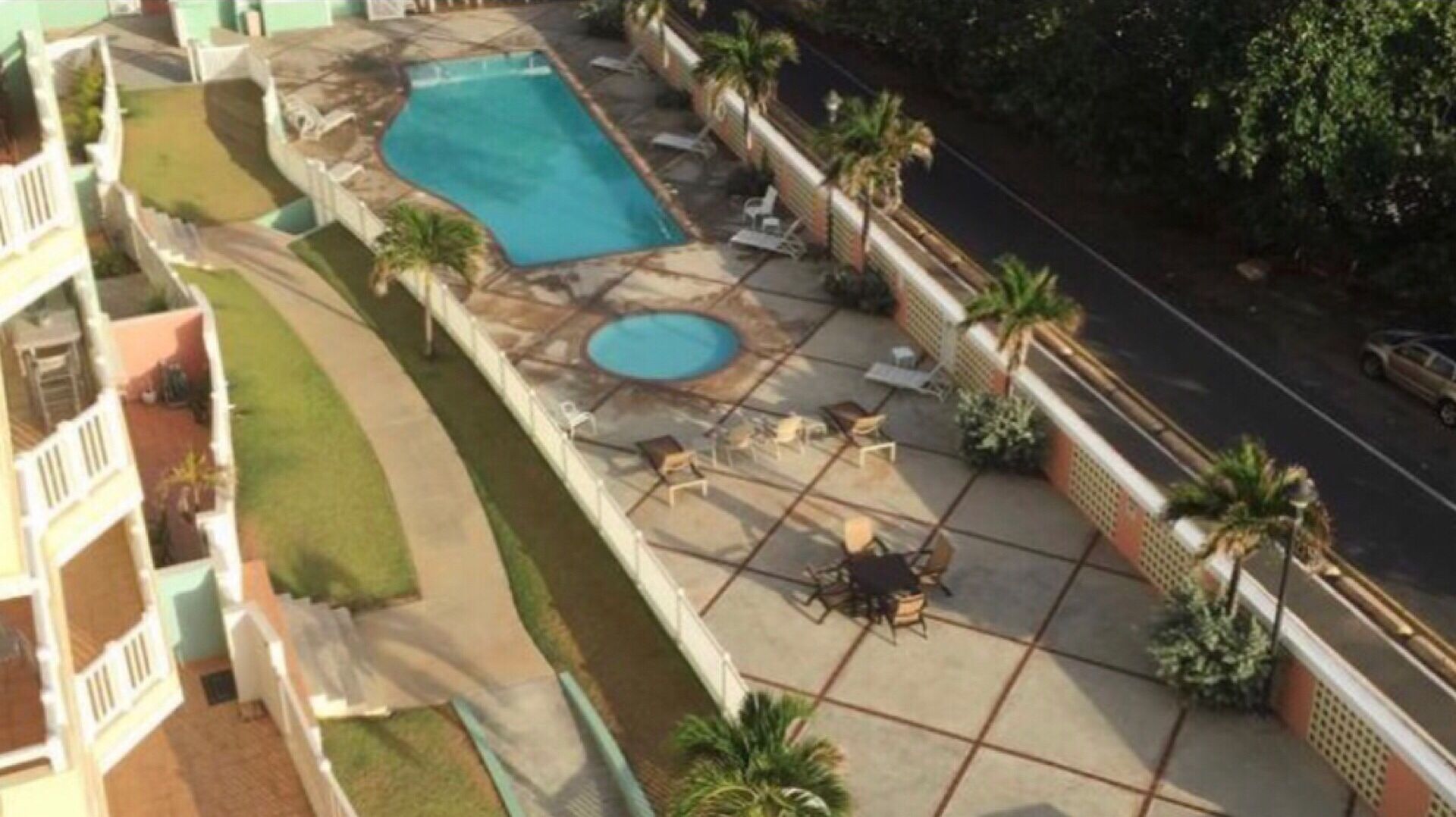 Un área de piscina en la azotea con piscina rectangular, jacuzzi, sillones de descanso y palmeras.