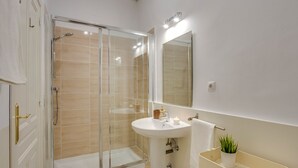 Een moderne badkamer met een douchecabine van glas, een wit wastafelmeubel met een spiegel erboven en een kleine plant in een potje op het aanrecht.