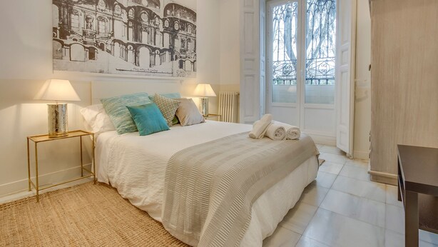 Een slaapkamer met een groot bed, twee bedlampen, een raam met uitzicht en een kunstwerk aan de muur.