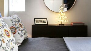 Ein Schlafzimmer mit Bett, Nachttisch mit Spiegel, Bilderrahmen und dekorativer Lampe.