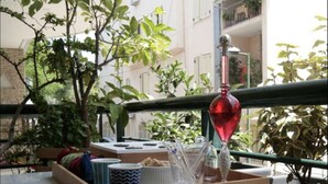 Ein Balkon mit Tisch, einem roten Dekoelement und Blick auf ein Gebäude mit Balkonen.