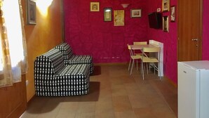 Ein Zimmer mit einer gepolsterten Couch, einem Esstisch mit Stühlen und einem Kühlschrank.