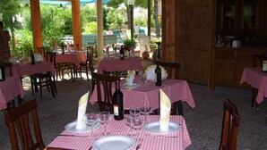 Ein Restaurant mit mehreren Tischen, die mit rot-weißen Karomustertischdecken bedeckt sind, Holzstühlen und bereitgestellten Weingläsern zum Speisen.