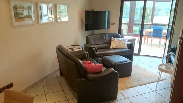 Een woonkamer met twee zwarte leren banken, een flatscreen-televisie aan de muur bevestigd, en een schuifdeur naar een buitenruimte met een tafel en stoelen.