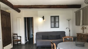 Una sala de estar acogedora con un sofá, sillas de madera, una mesa de comedor con mantel blanco, una lámpara y una ventana con cortinas.