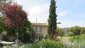 Una casa de piedra con tejado de tejas, rodeada de un jardín con diversas plantas y flores.