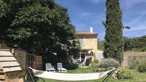 Una hamaca en un patio con césped, un edificio de piedra y un árbol alto.