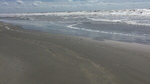 A beach with a wide sandy shore and waves approaching the beach.