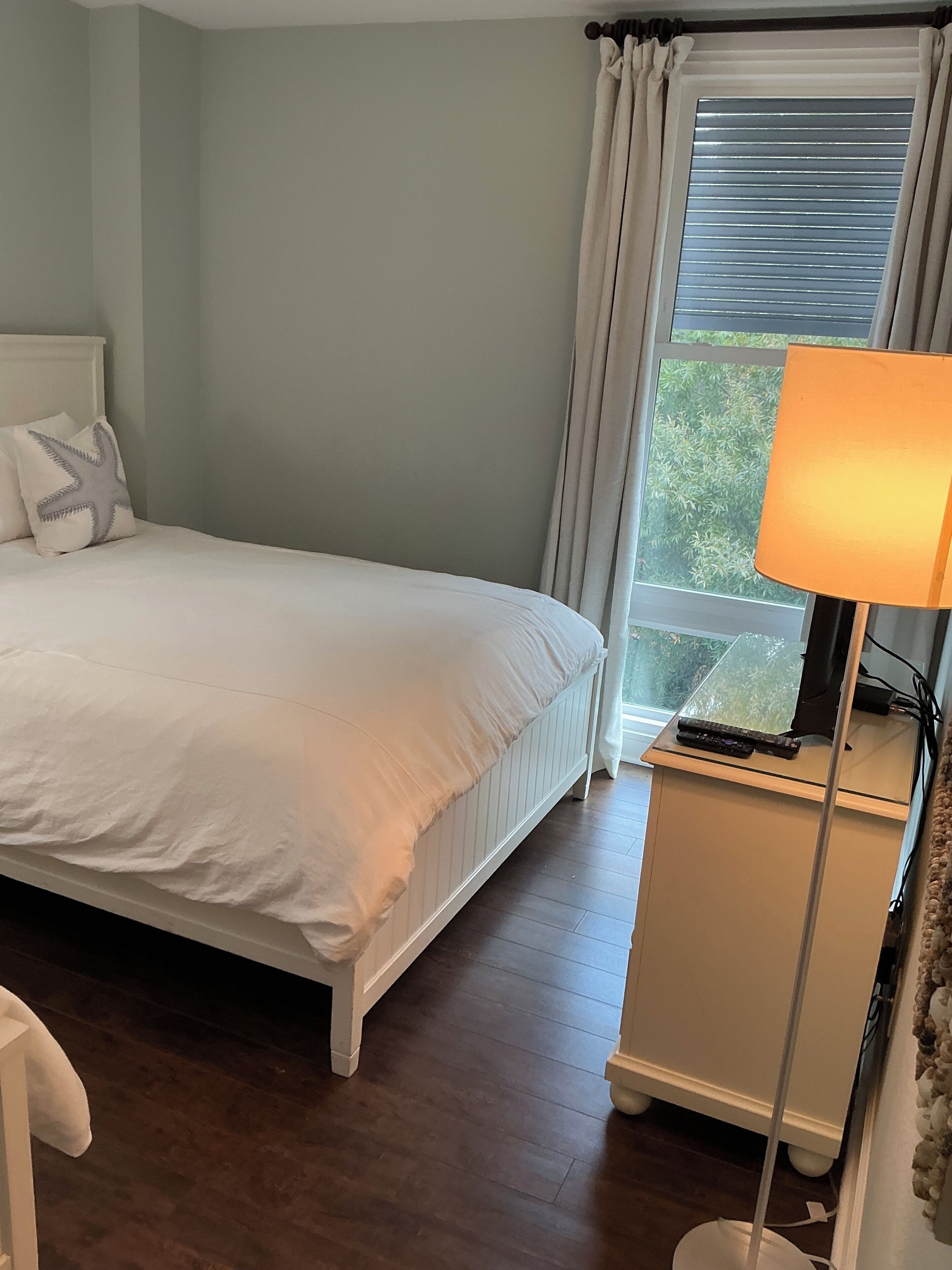 Une chambre à coucher avec un lit, une table de chevet, une lampe et une fenêtre avec des rideaux.