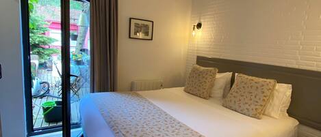 A bedroom with a bed, a nightstand, a window with curtains, a wall-mounted light, and a radiator.
