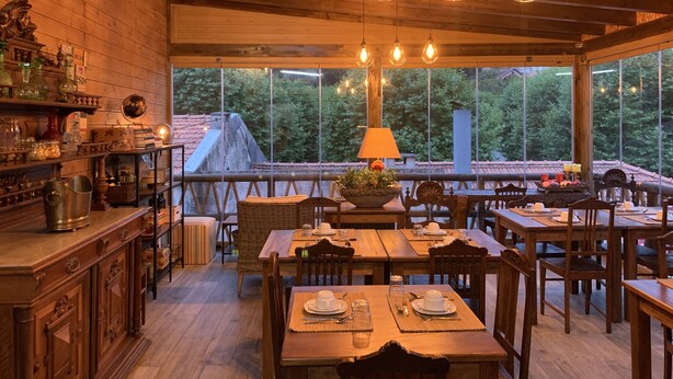 A cozy wooden interior with a dining area, wooden shelves with glassware, and a view of greenery outside. - Storytellers Villas (Sintra)