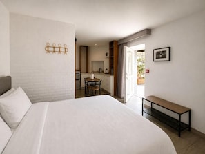 A hotel room with a large bed, a small table, a bench, a kitchenette, and a bathroom visible through an open door. - Storytellers Villas (Sintra)