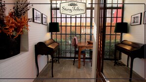 A room with a wooden bench, a table, and chairs, a vase with flowers, and a sign reading "Story Tellers". - Storytellers Villas (Sintra)