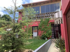 Um edifício vermelho com varanda, janela e um pequeno jardim com grama e plantas.