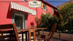 A red building with a sign reading "Story Tellers" and a patio with wooden furniture. - Storytellers Villas (Sintra)