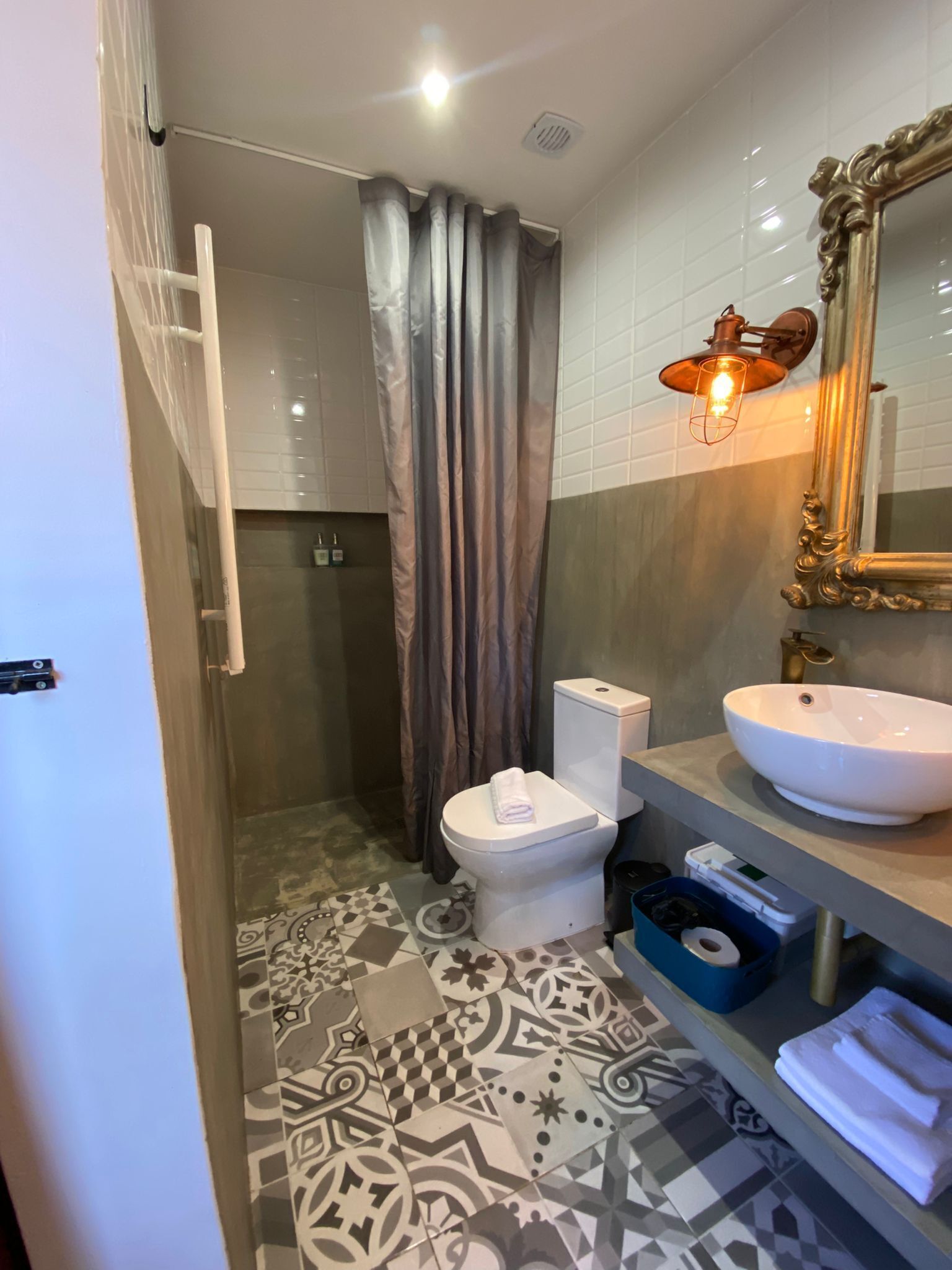 Een badkamer met toilet, wastafel, douchegordijn, vloertegels met patroon en een spiegel aan de muur.