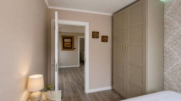 A bedroom with a bed, bedside table with a lamp, a wardrobe, and a door leading to another room.