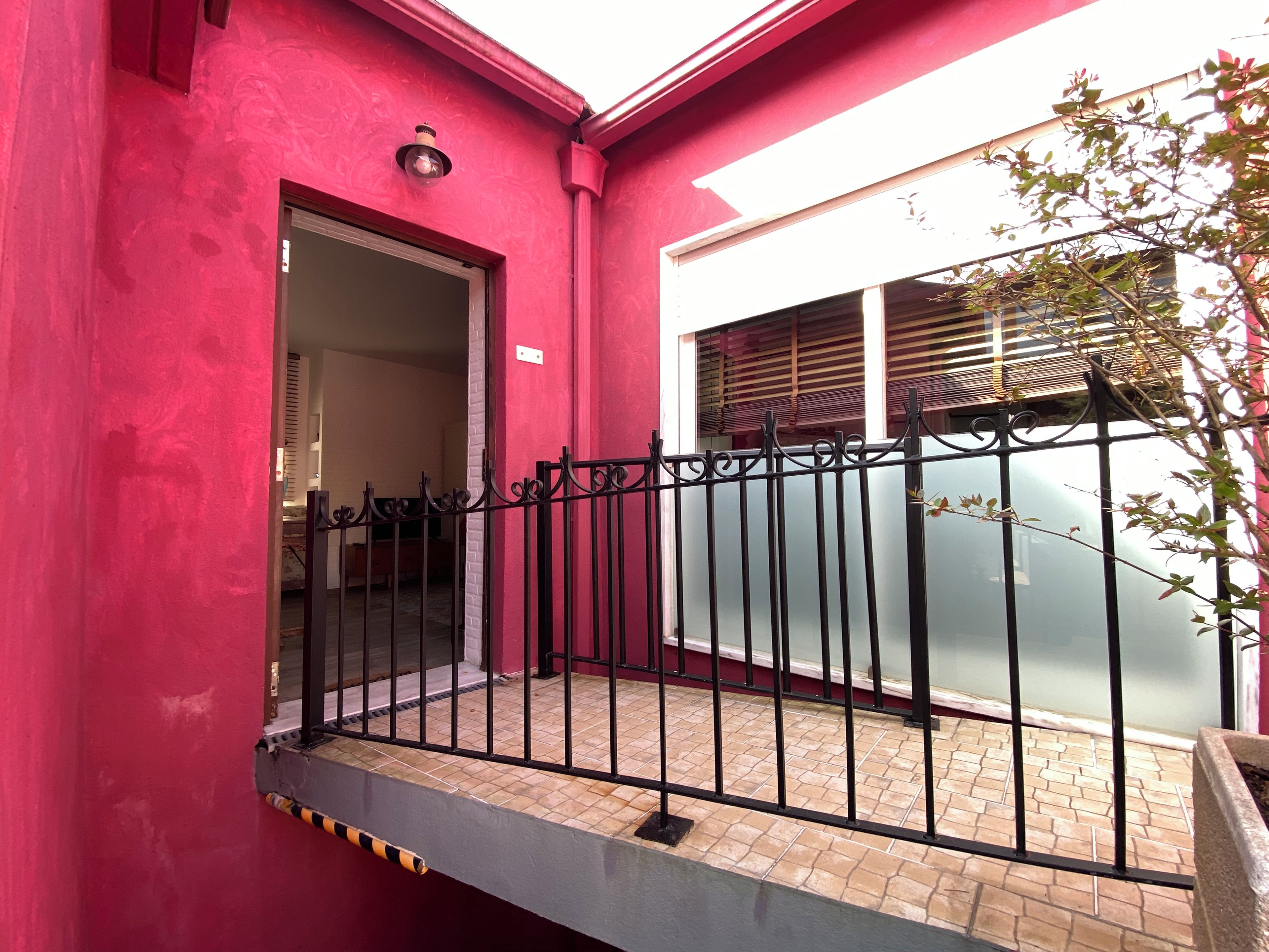 Un edificio rojo con una cerca de metal negro, una puerta y una ventana con persianas.