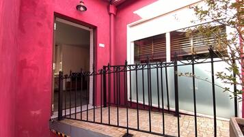 Un edificio rojo con una cerca de metal negro, una puerta y una ventana con persianas.